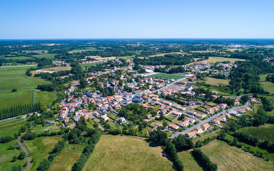 Luftaufnahme einer ländlichen Ortschaft, umgeben von Feldern, Wiesen und weitläufiger Landschaft.