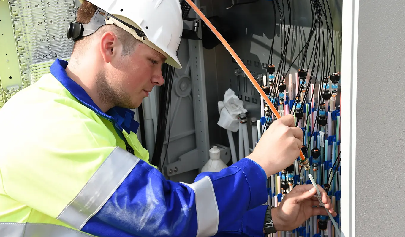 Ein Mitarbeiter bringt einen Rohradapter wird an einem Verteilerschrank an.