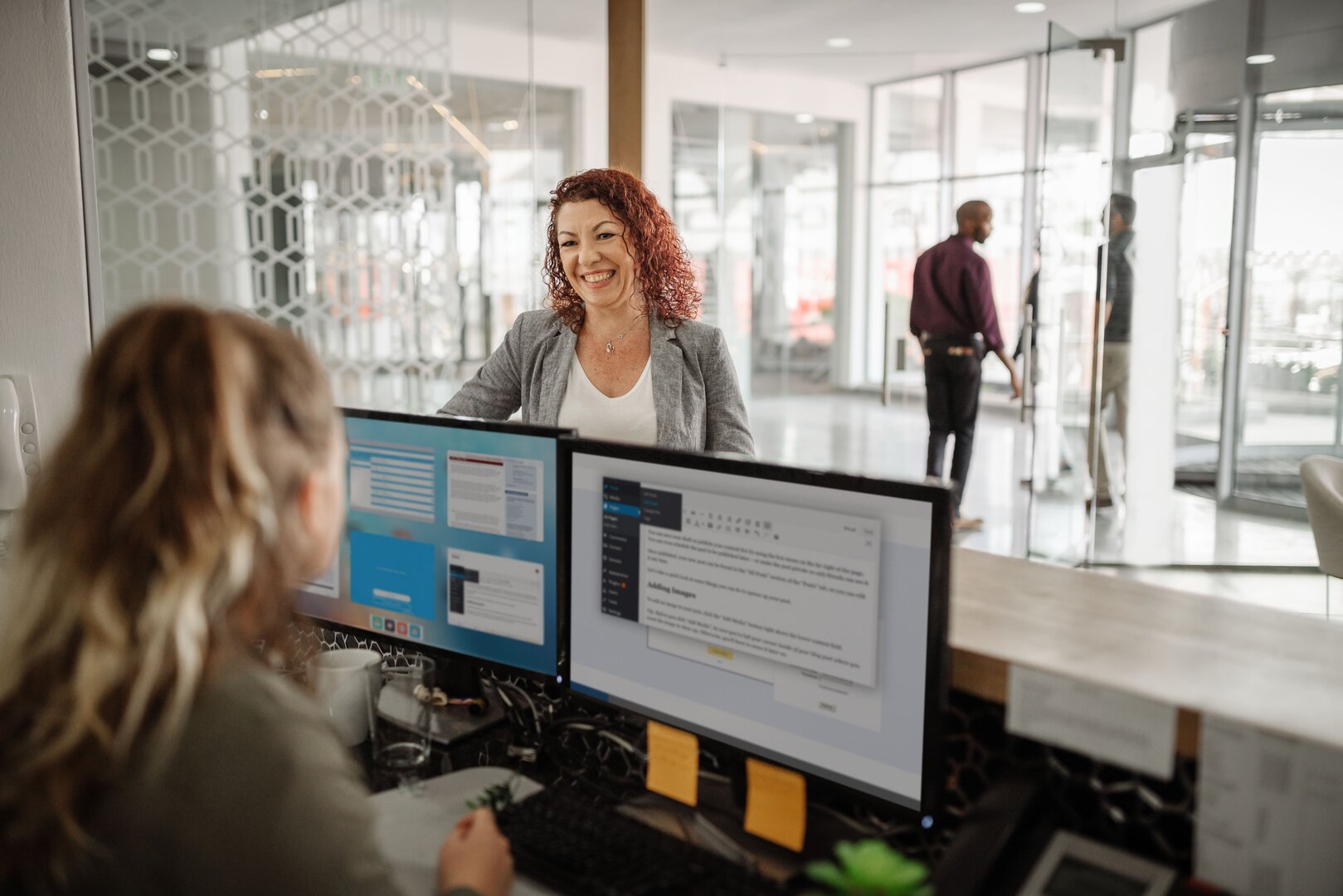 Mitarbeiterin am Empfang spricht mit einer Kundin in einem modernen Büro.