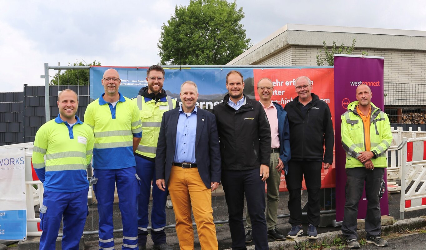 Auf dem Foto sind acht Personen zu sehen, darunter Thomas Schwefer (Westnetz), Heiko Grebe (Westconnect), Adiran Biggeleben (Westnetz), Wolf Blesken (Bürgermeister Gemeinde Möhnesee), Johannes Kobeloer (Westenergie), Klaus Peter Teipel (Ortsvorsteher Körbecke), Jürgen Schmitt (Leiter Fachbereich Gemeindeentwicklung Möhnesee) und Maksym Zakharov (Tiefbauunternehmen MDNetworks).