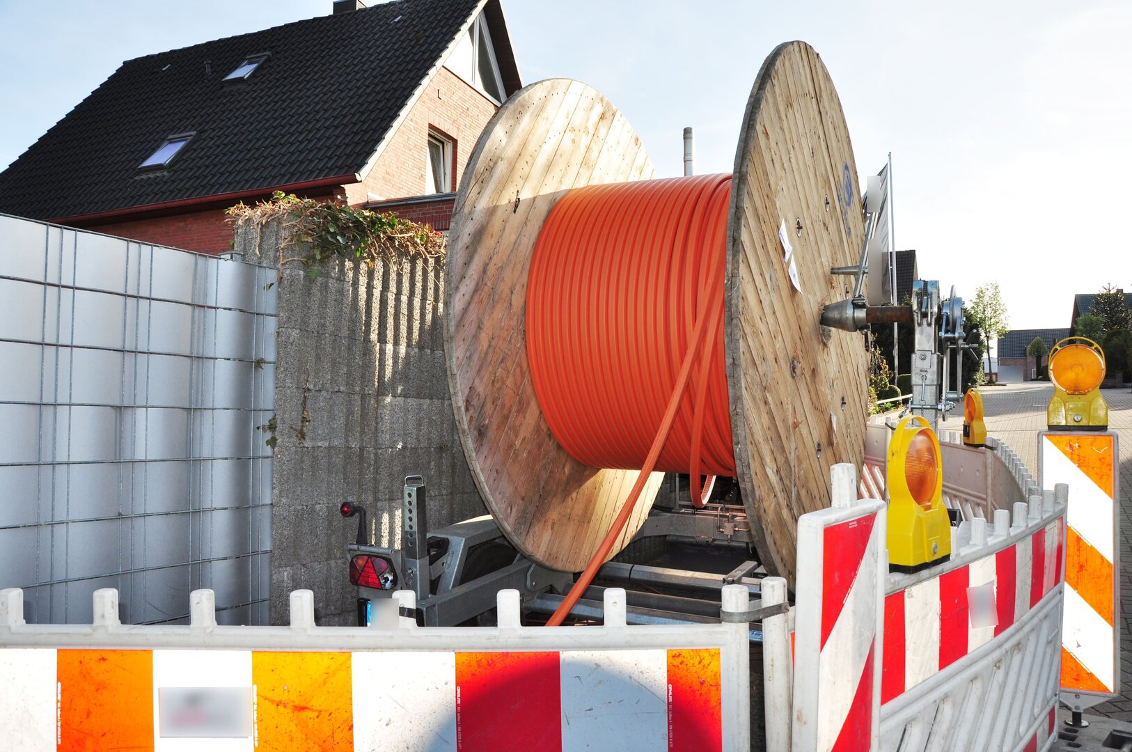 Große Trommel mit orangefarbenem Leerrohr für den Glasfaserausbau auf einer abgesperrten Baustelle.