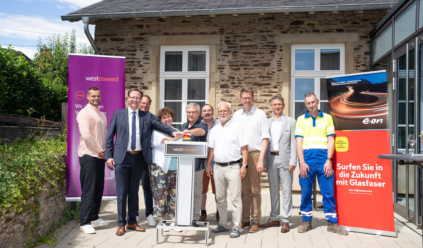 Auf dem Foto sind zehn Personen zusehen, darunter Kevin Schwiderski (Landkreis Bernkastel-Wittlich), Andreas Hackethal (Landrat des Landkreises Bernkastel-Wittlich), Sven Bender (Westconnect GmbH), Beatrix Kimnach (Ortsvorsteherin Wolf), Edgar Langen (stellv. Ortsvorsteher), Edgar Koch (3. Beigeordneter Stadt Traben-Trarbach), Patrice-Christian-Roger Langer (Stadtbürgermeister Traben-Trarbach), Marcus Heintel (Bürgermeister Verbandsgemeinde Traben-Trarbach), Marco Felten (Westenergie AG) und Andreas Müller (Westnetz GmbH).