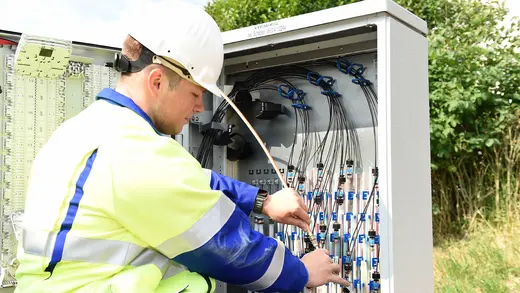 Ein Mitarbeiter bringt einen Rohradapter wird an einem Verteilerschrank an.