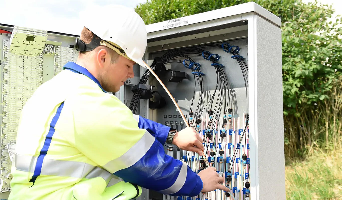 Ein Mitarbeiter bringt einen Rohradapter wird an einem Verteilerschrank an.