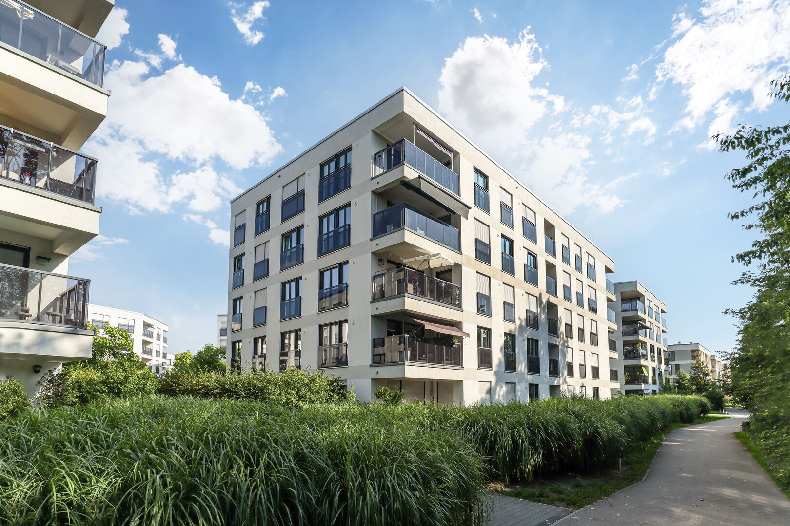 Modernes mehrstöckiges Wohngebäude in einem Neubauquartier mit begrünten Wegen und Balkonen.